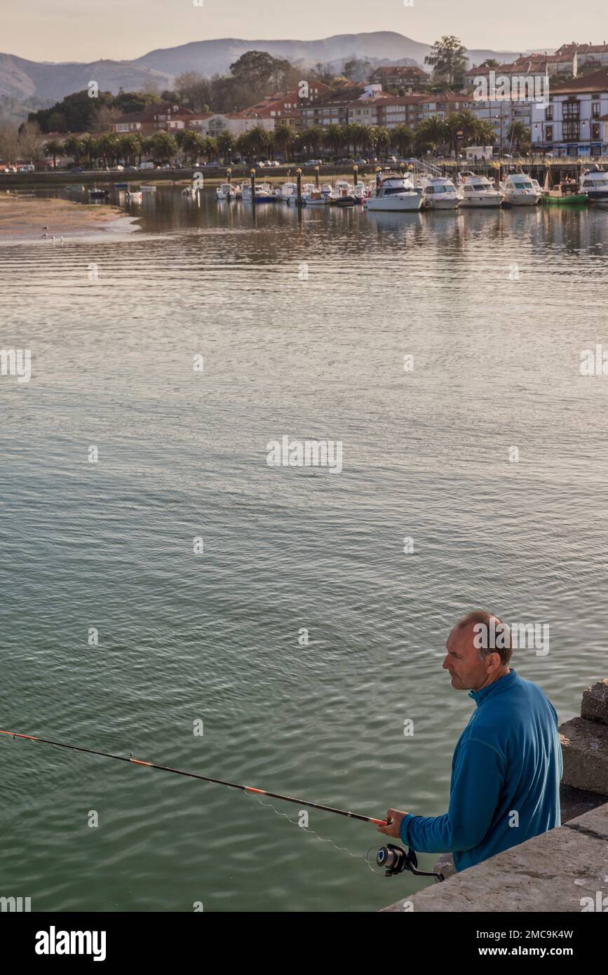 Man fishing with a rod in the ria of San Vicente de la Barquera with the marina and fishing port in the background, Cantabria, Spain, Europe Stock Photo