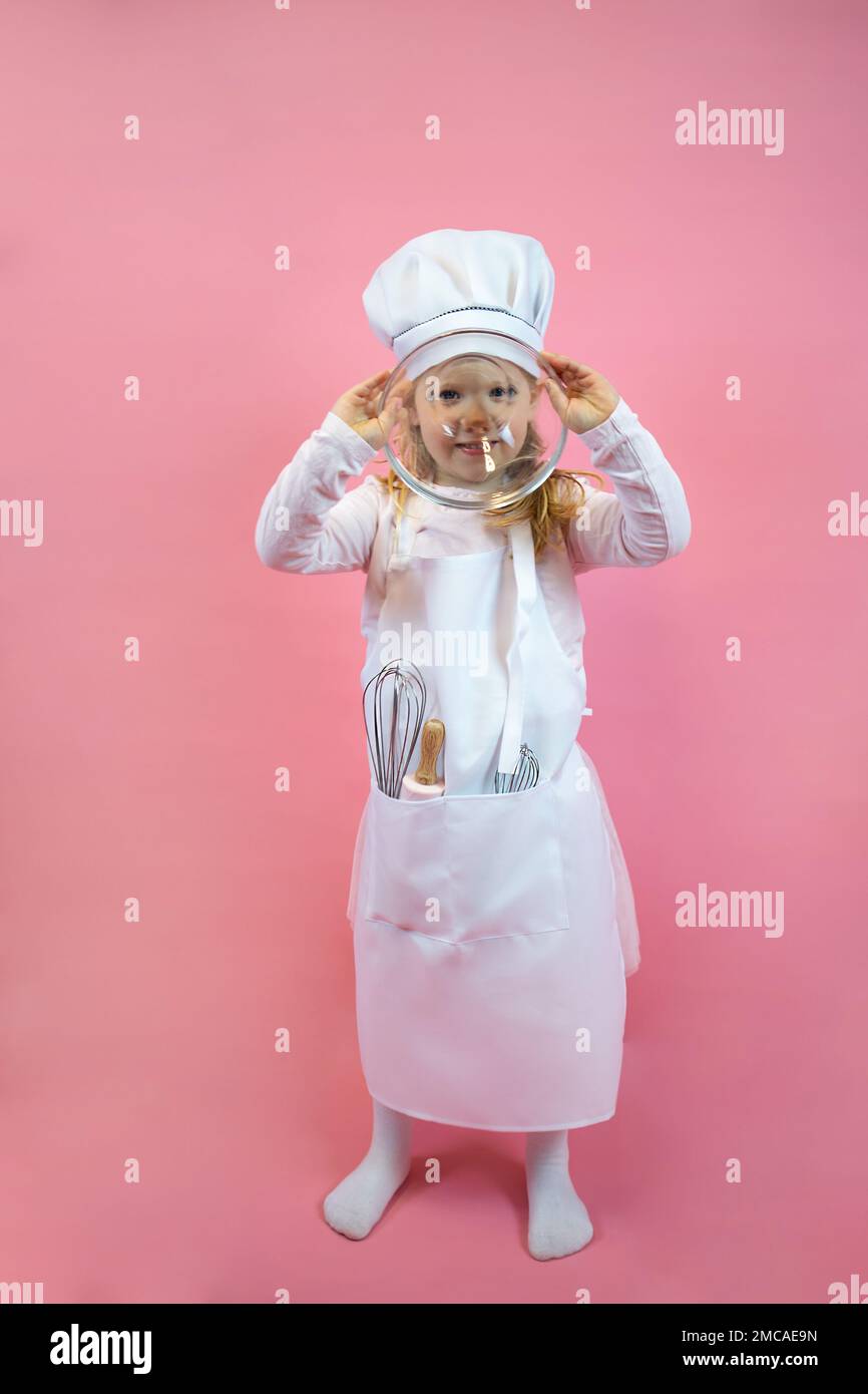 Little cook girl in an apron and cap, holds a glass cup and covers her face Stock Photo