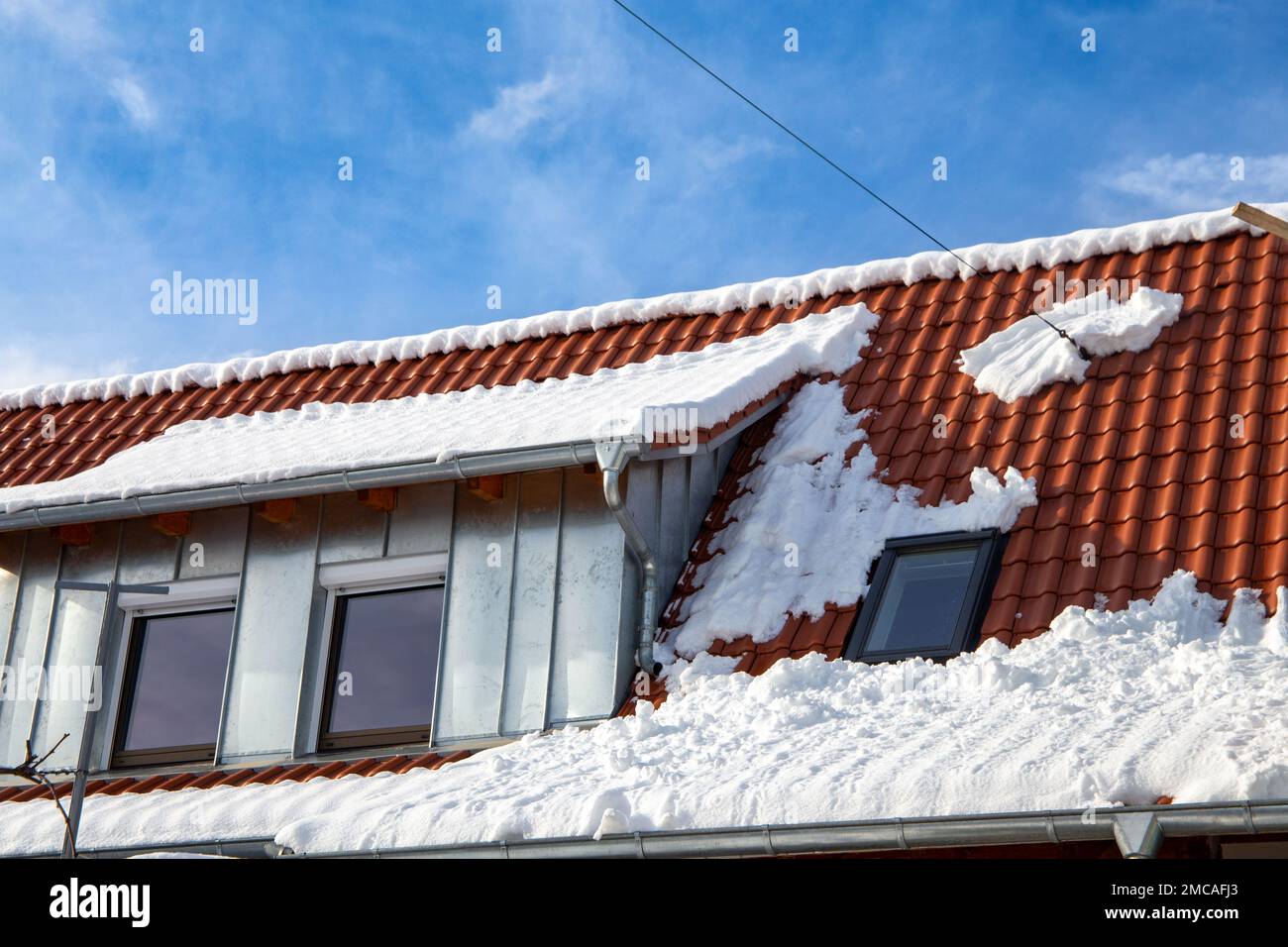 Symbol image of roof avalanche: Snow sliding down the tiled roof of a residential building Stock Photo