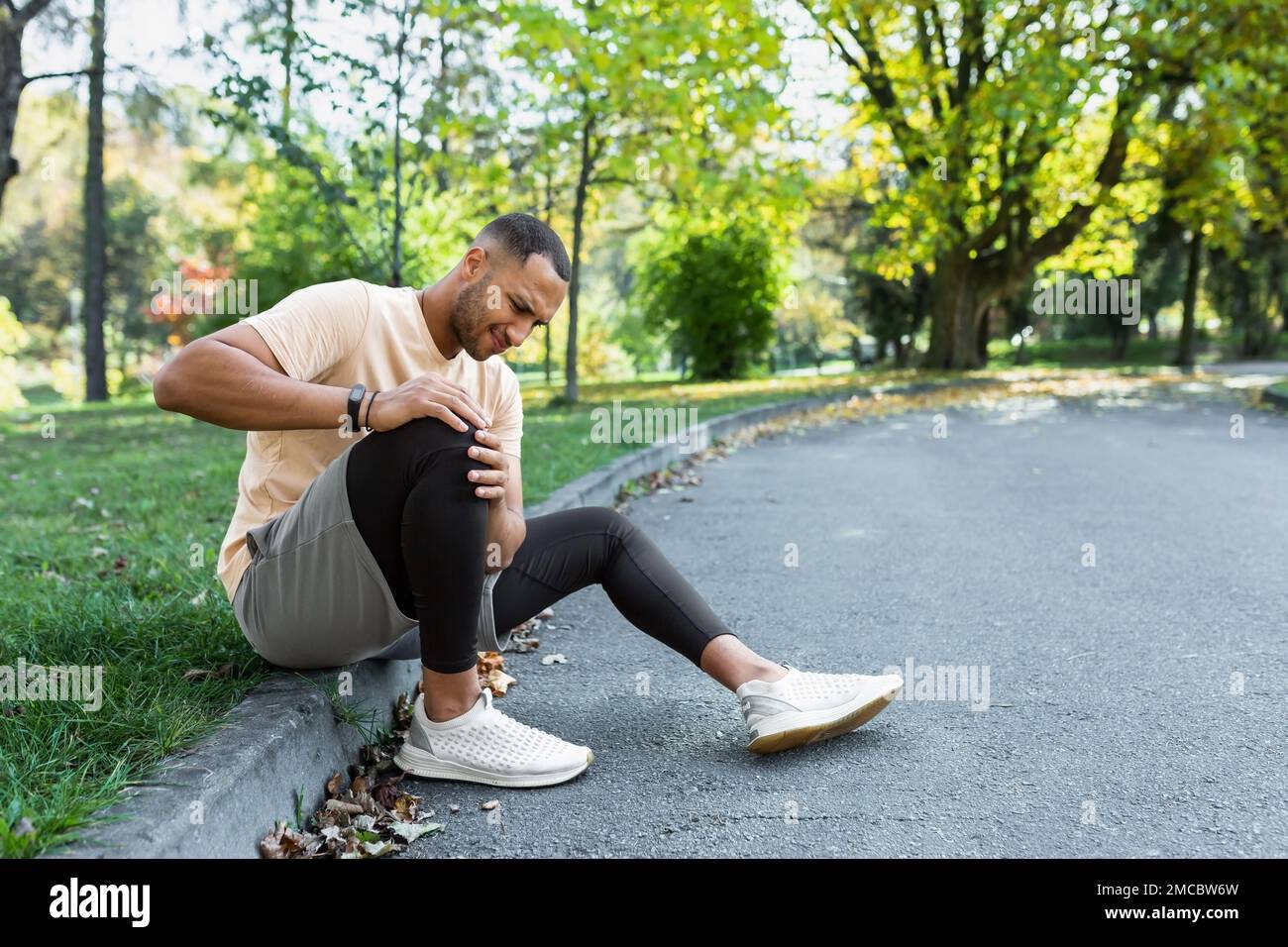 Man injured leg while jogging, african american man sitting on ground
