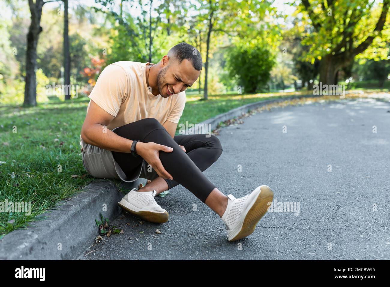 Man injured leg while jogging, african american man sitting on ground