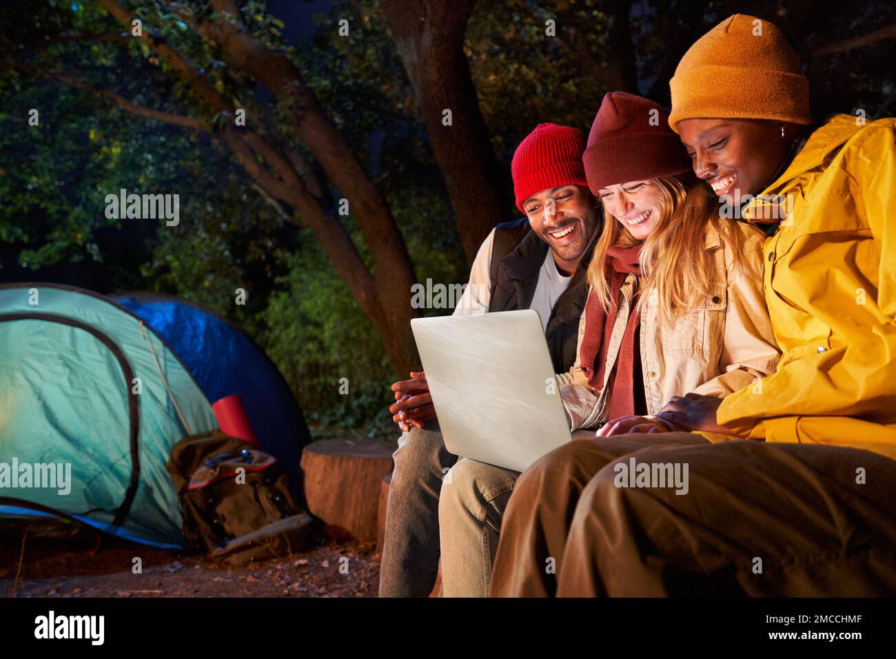 Friends using computer during camping together on winter night. Stock Photo
