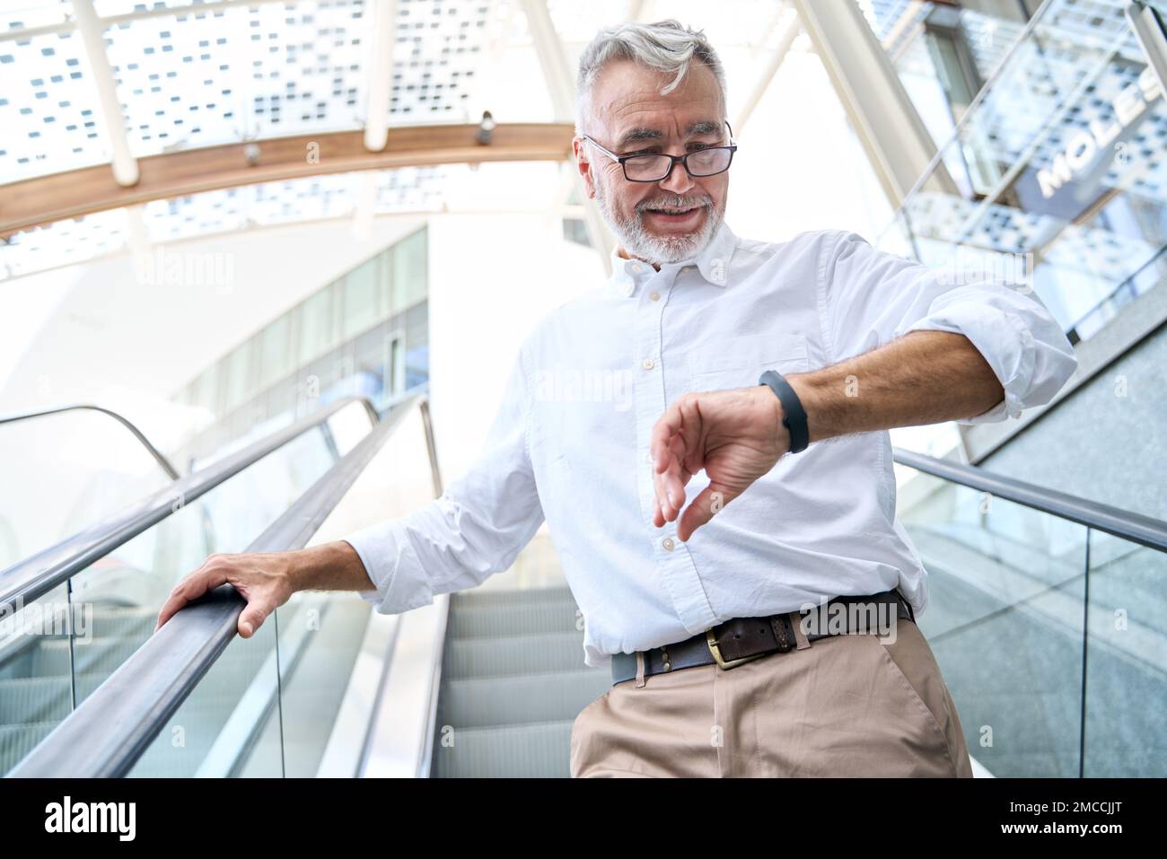 Older senior business man looking at wristwatch or fitness tracker outdoors. Stock Photo