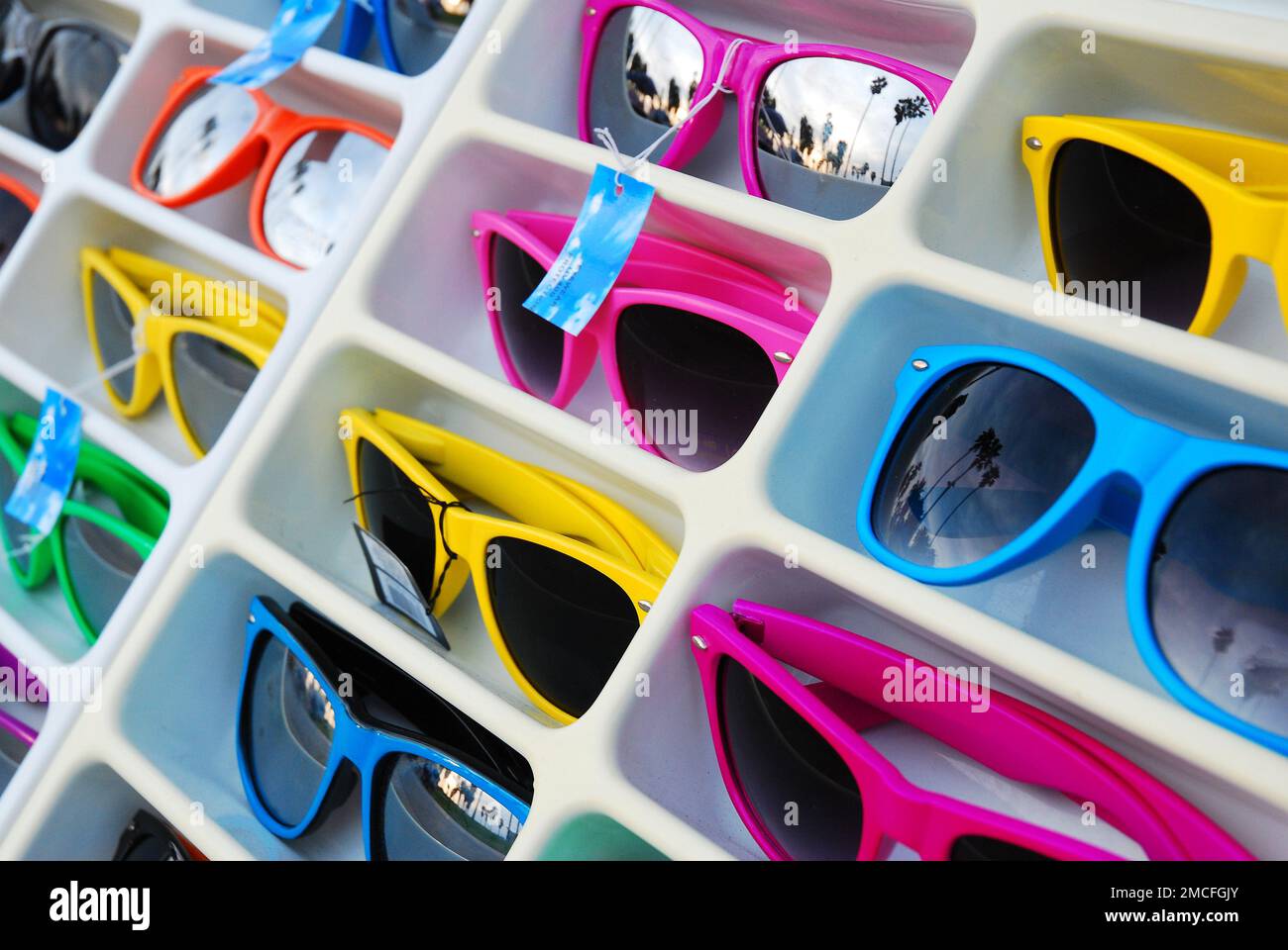 Colorful sunglasses on display at an outdoor market stall and retail store, reflecting palm trees, foreshadow a sunny day at Venice Beach, California Stock Photo
