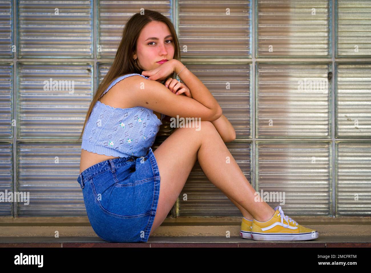 Teenage Girl Sitting in Front of Window Made of Art Deco Glass Bricks Side View Stock Photo
