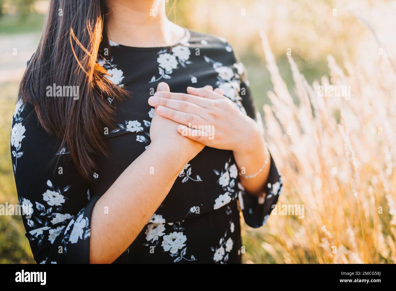 Hopeful woman putting hands on her chest in gratitude for God's blessings, in the field. Copy space Stock Photo