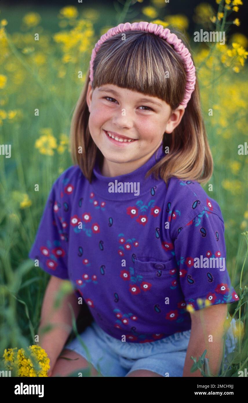 Young girl sitting out in fields of tallgrass and yellow flowers posed