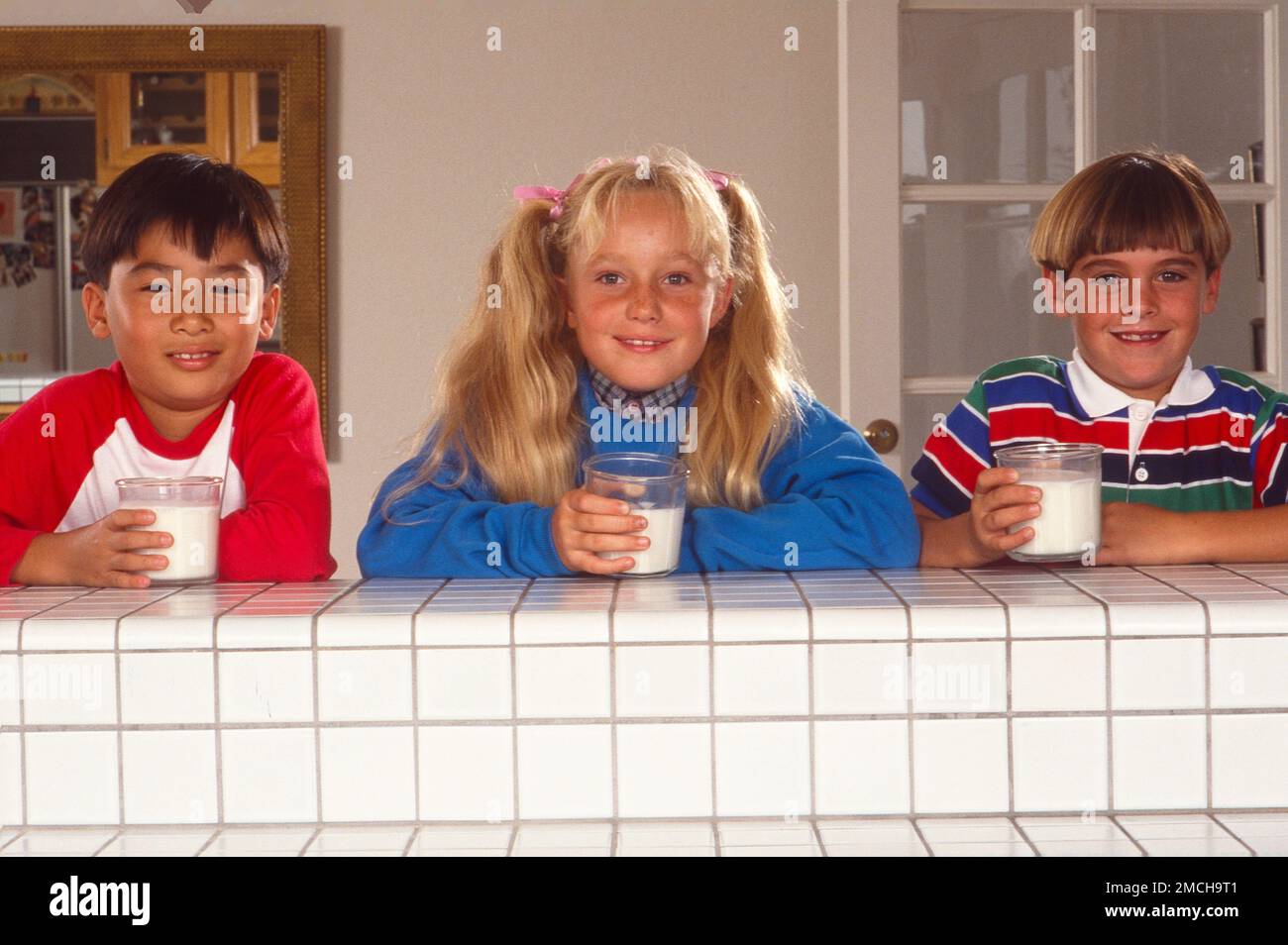 Three children standing behind a wall, each holding a glass of milk ...