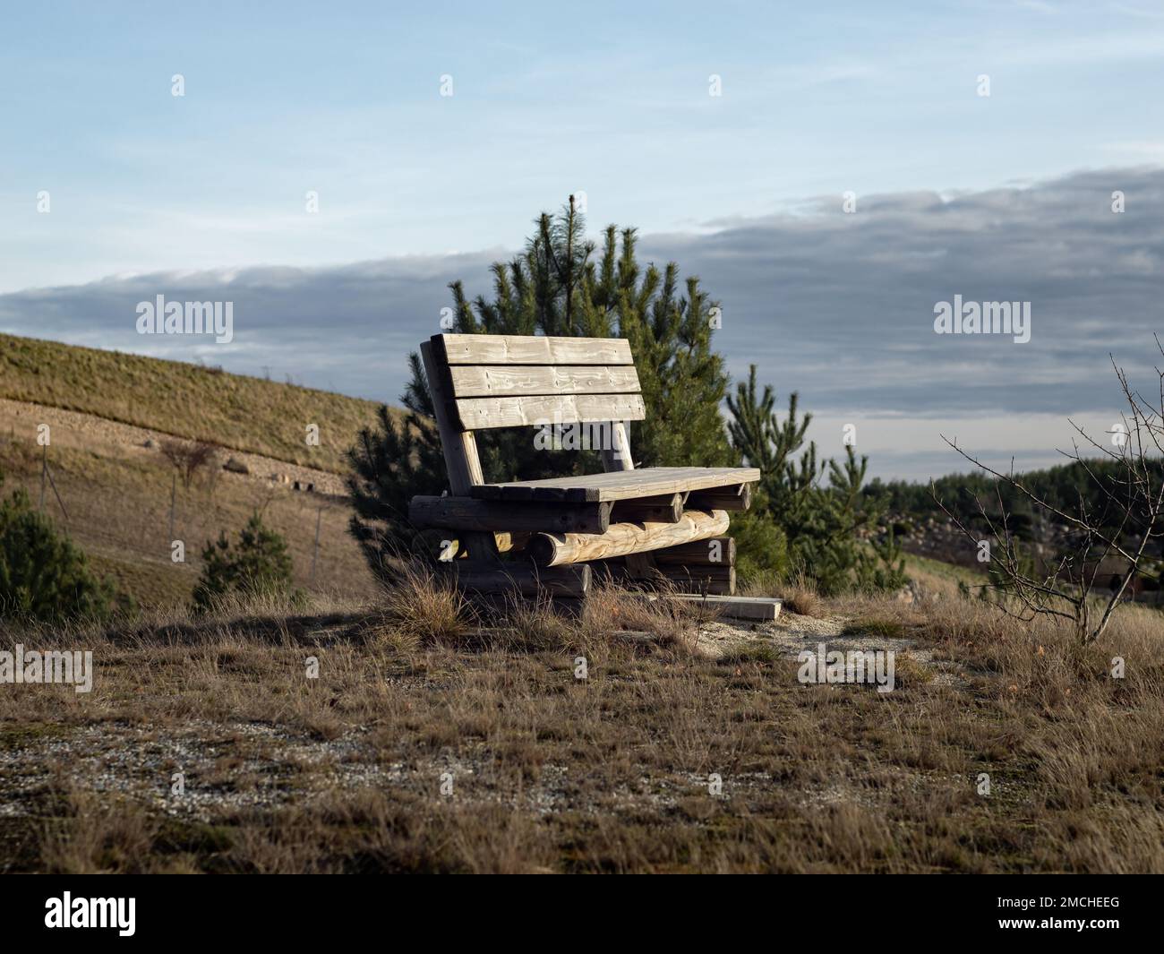 Empty park bench on top of a hill in the nature. The calm and idyllic landscape is in the background. Nice place to rest in a rural area. Stock Photo