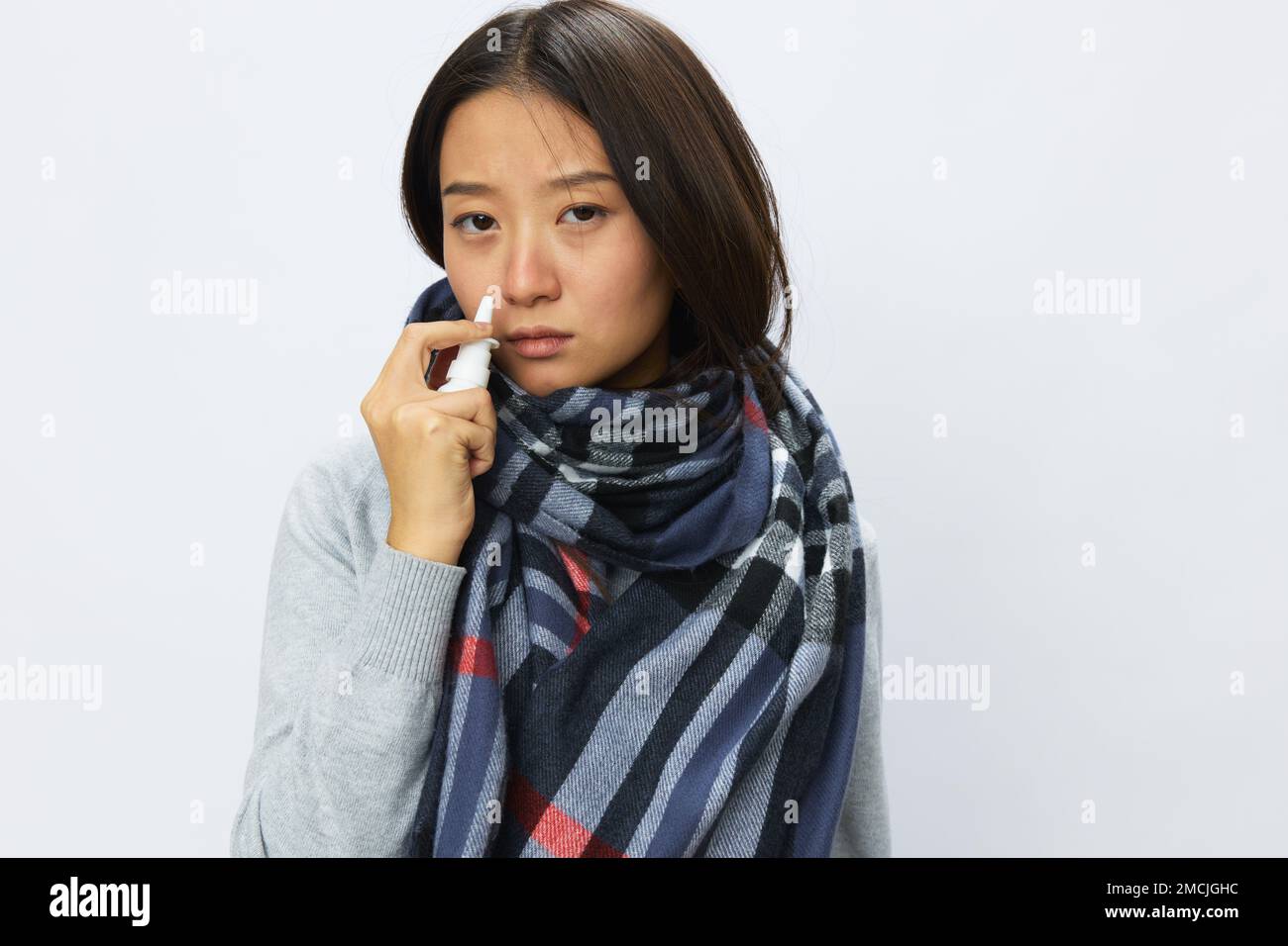 Asian woman flu cold with stuffy nose holds nasal spray and sprays