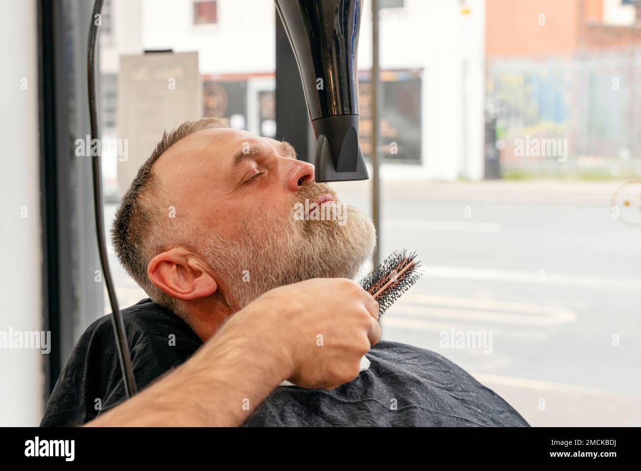 Barber trimming and cutting bearded man with shaving machine in