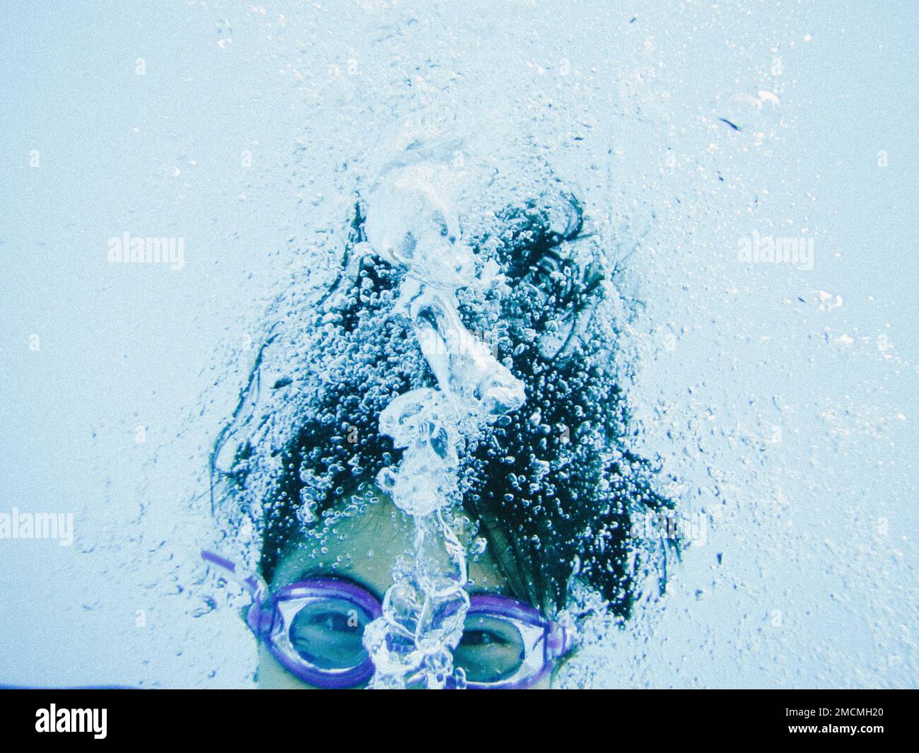 Girl swimming underwater wearing goggle with lots of air bubbles Stock