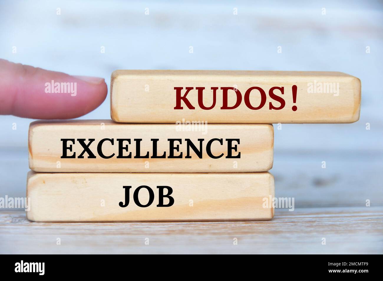 Finger pointing KUDOS text on wooden blocks with wooden cover background. Achievement concept