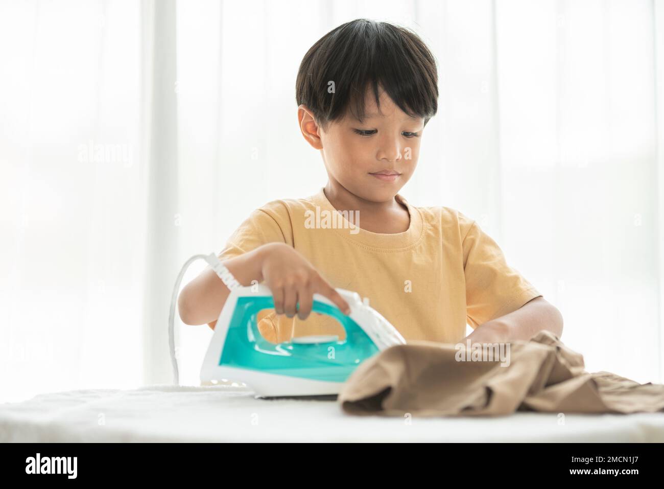 young happy boy iron his school uniform with iron on iron board at home