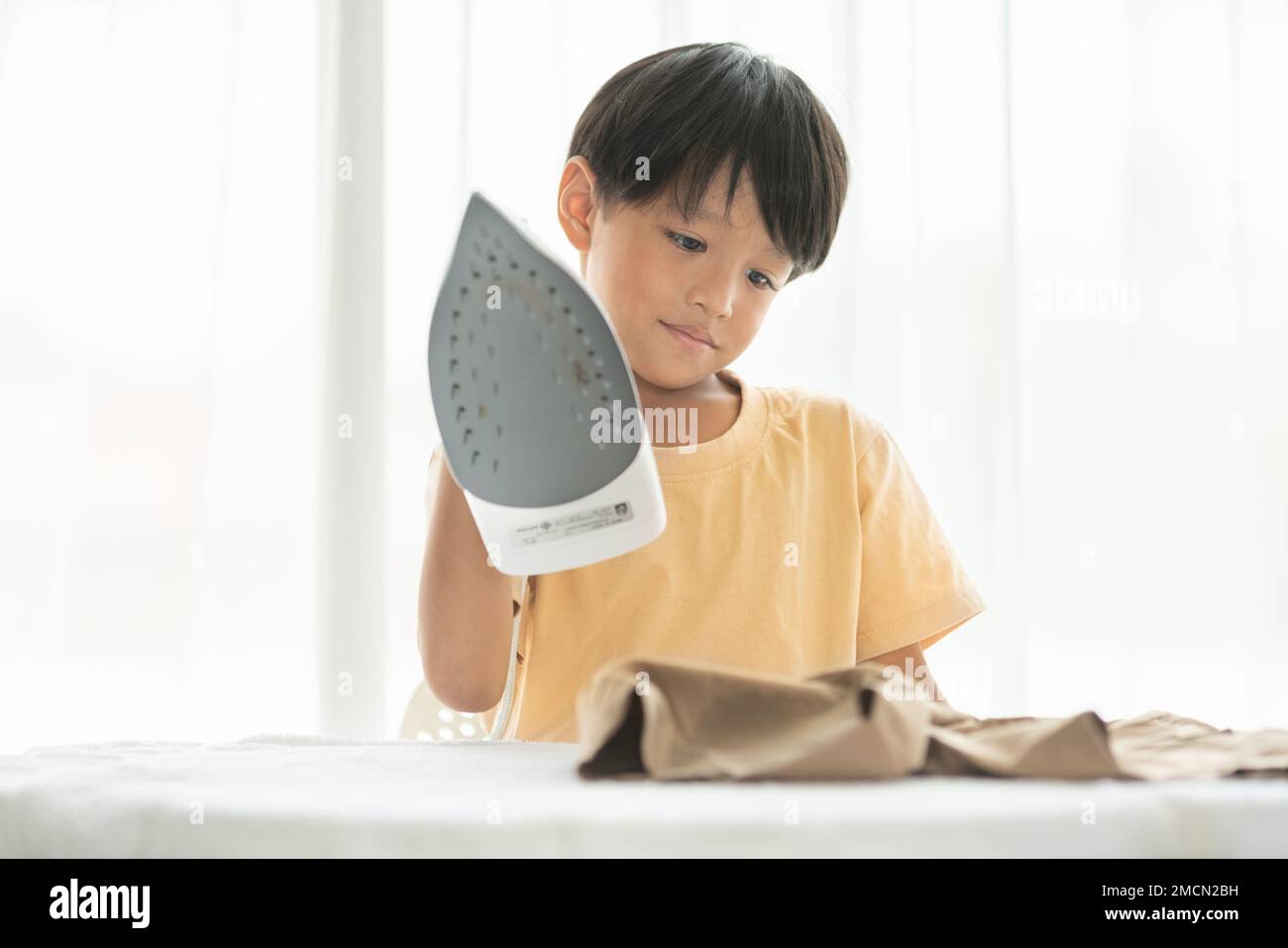 young happy boy iron his school uniform with iron on iron board at home