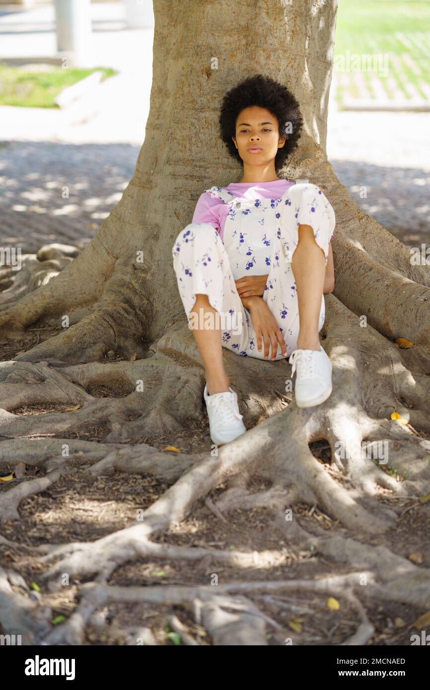 Pensive black woman sitting near tree Stock Photo