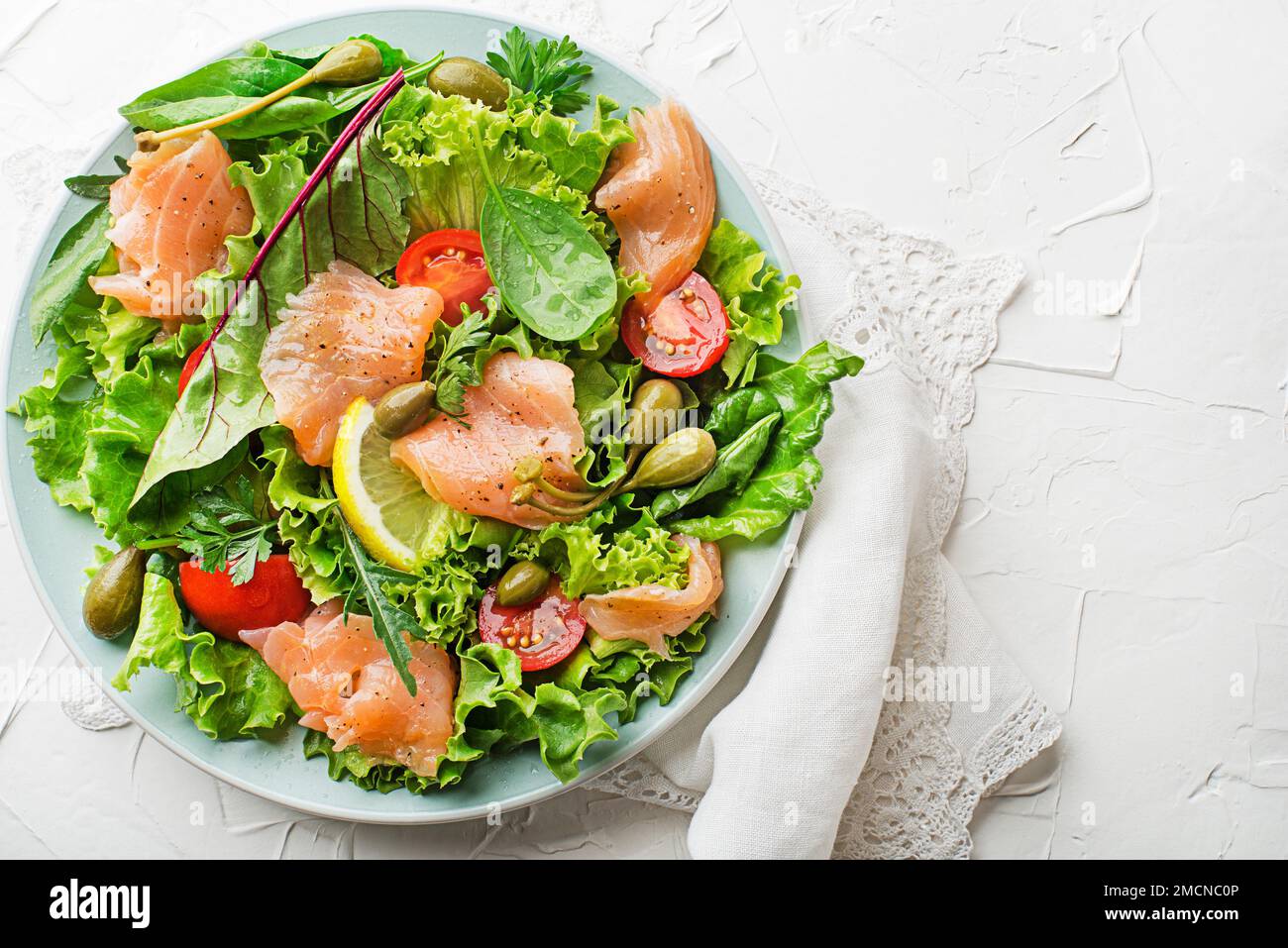 Fresh green salad with smoked salmon, cherry tomatoes and capers on white table background close up Stock Photo