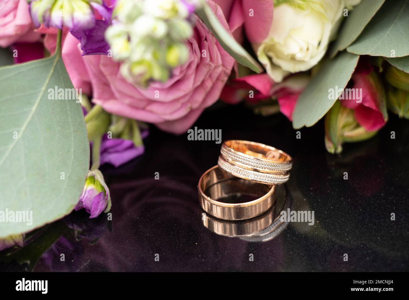 two wedding gold rings on a dark mirror background carried a bouquet of flowers, wedding gold rings, wedding Stock Photo