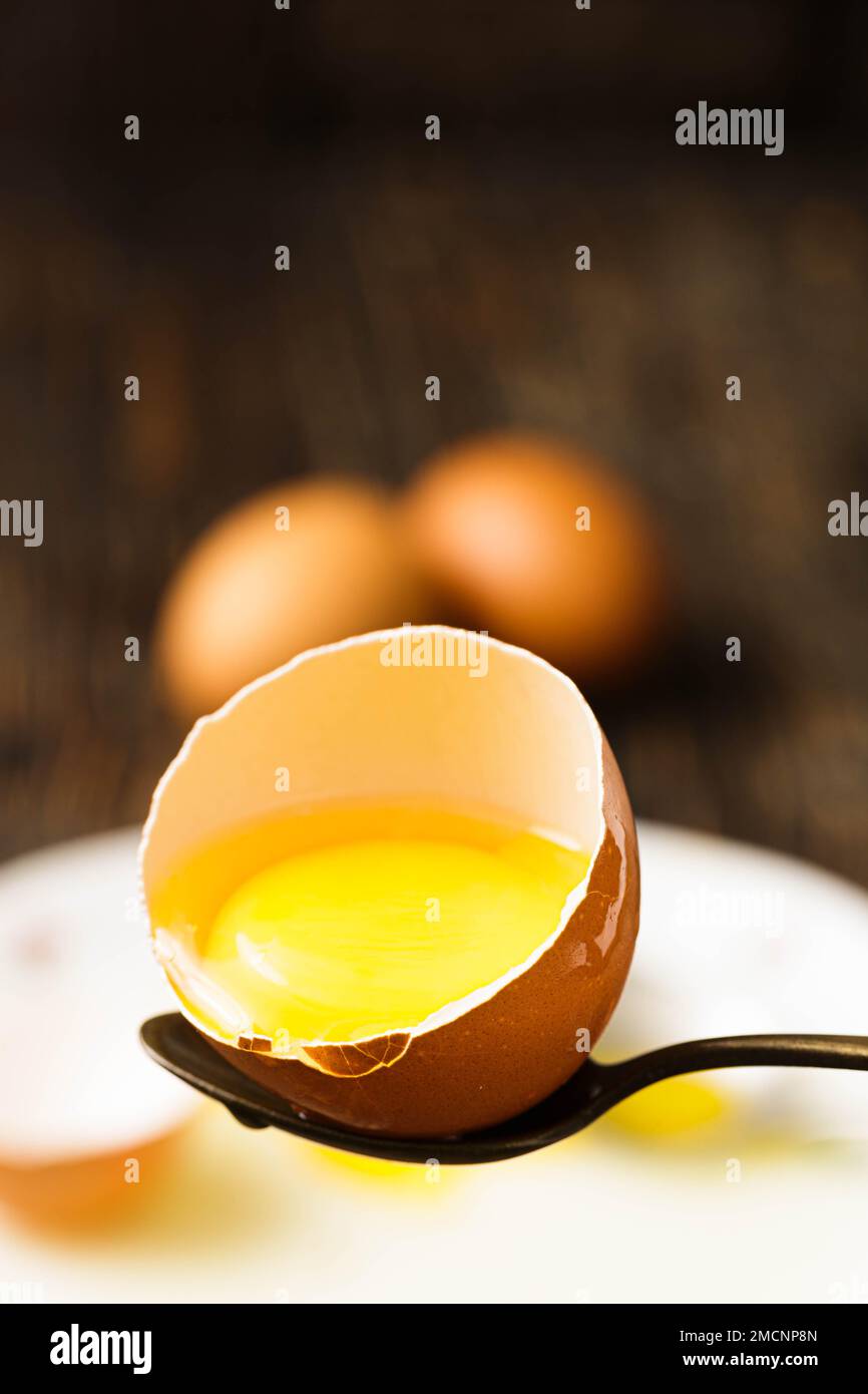Half-cut raw egg on spoon, yolk visible, golden yellow, surrounded by egg white, spoon as utensil. Stock Photo