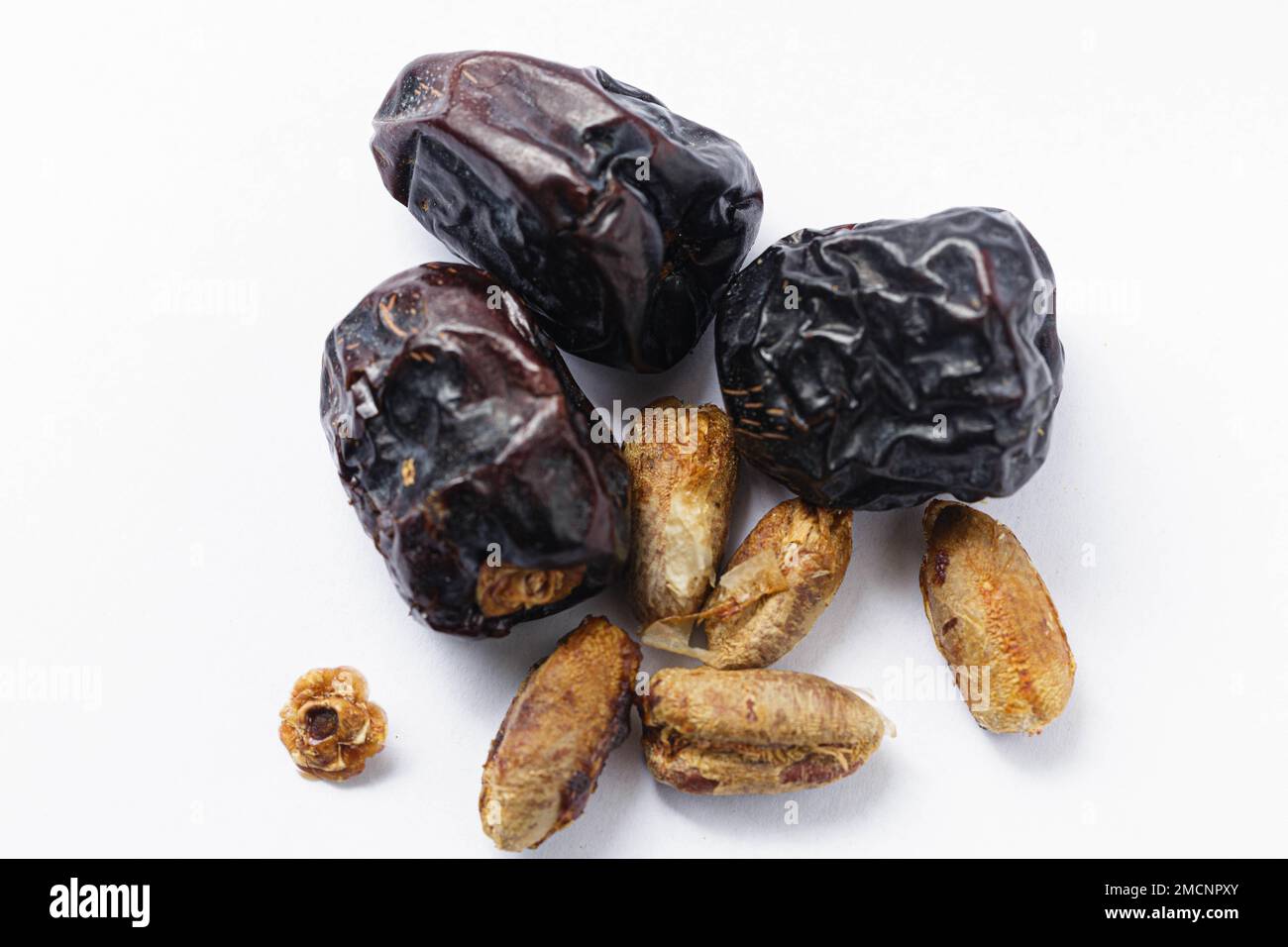 The rich dark-brown color and unique shape of Ajwa dates stand out against the white background Stock Photo