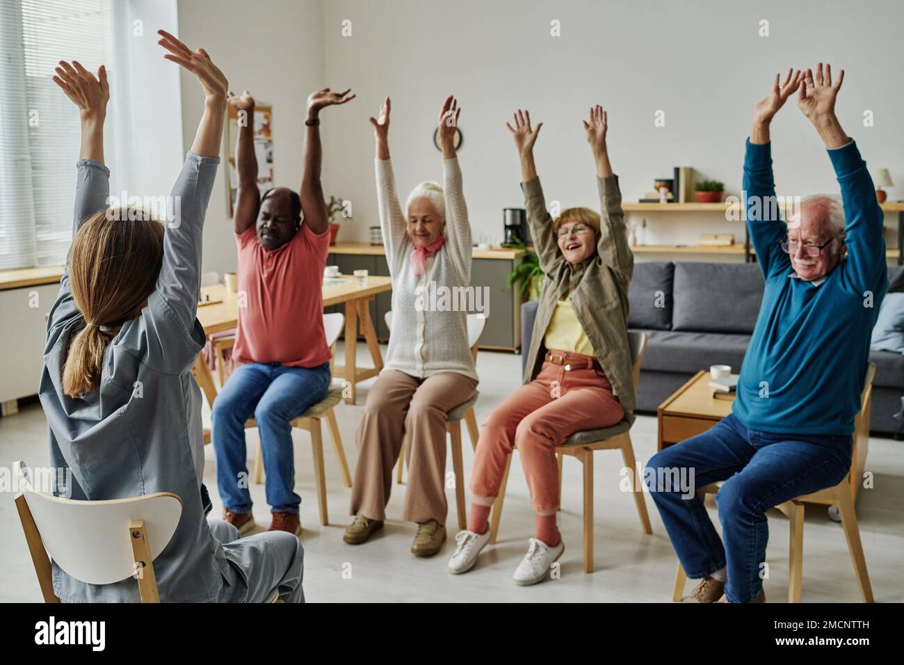 Group of senior people sitting on chairs and exercising during sport training with instructor