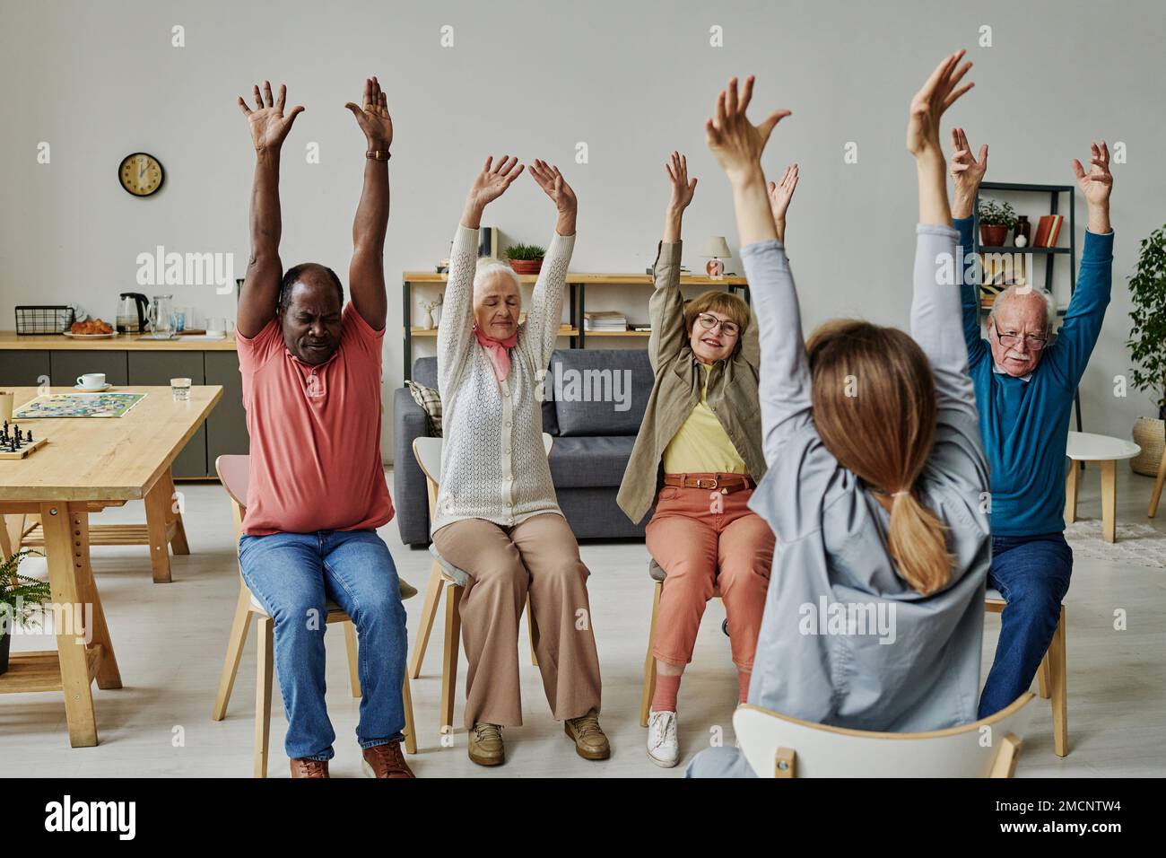Group of senior people sitting on chairs and repeating exercises