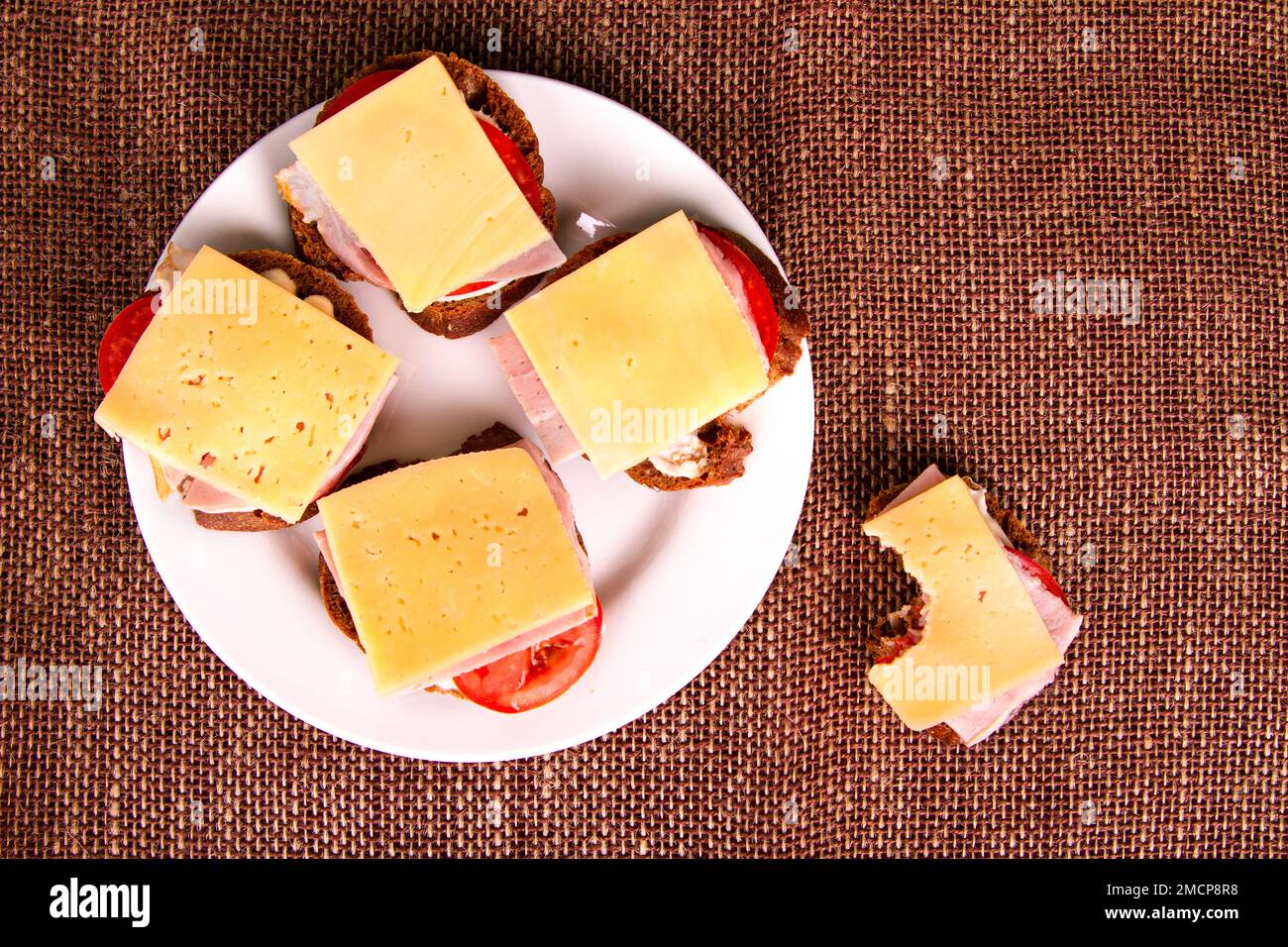 Top view of bitten sandwich with rye bread, tomatoes, ham and cheese on