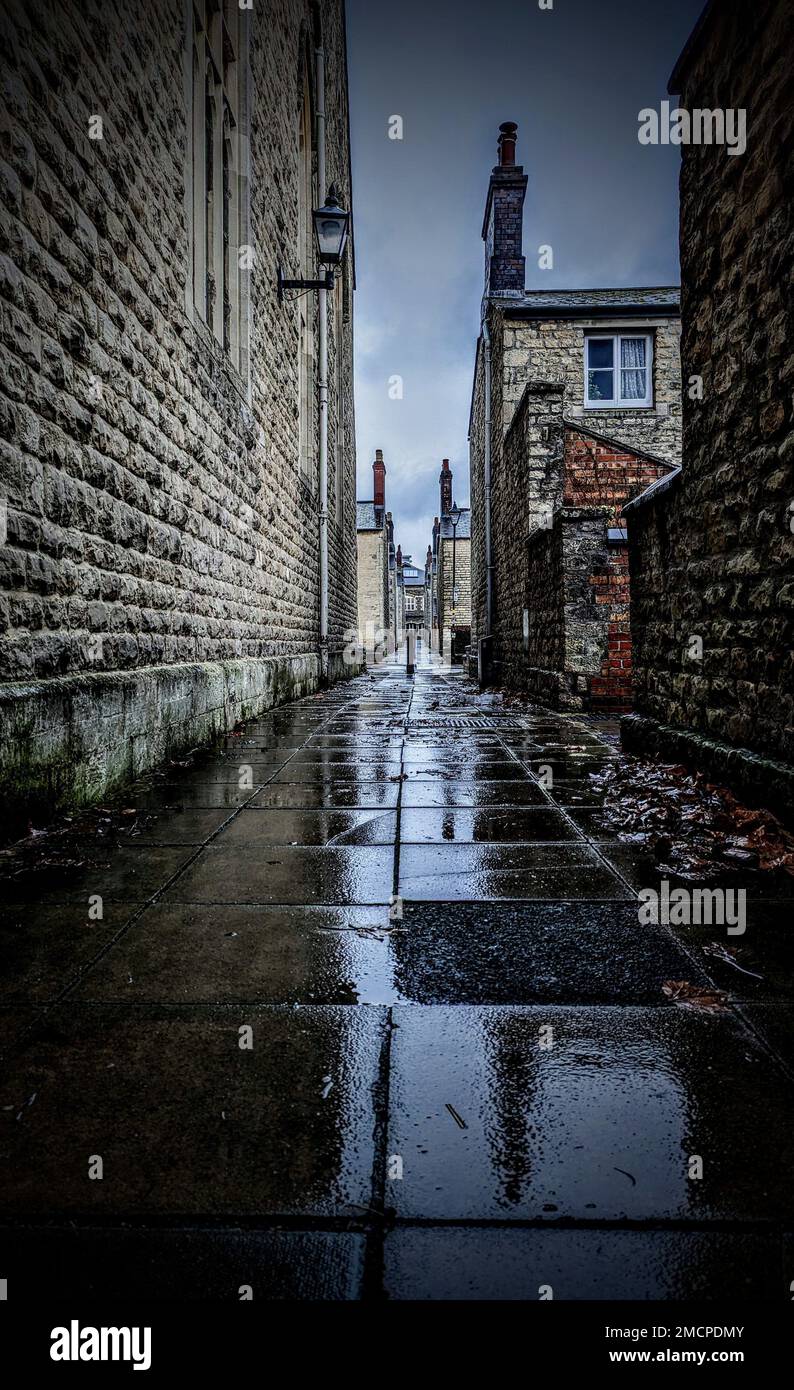 A vertical shot of a narrow street between brick buildings after rain ...