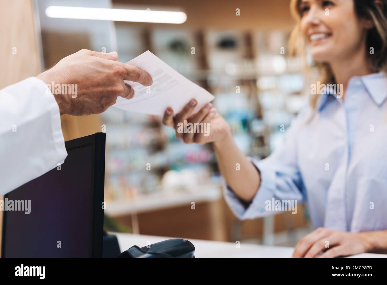 Patient handing a pharmacist a doctor's prescription in a chemist