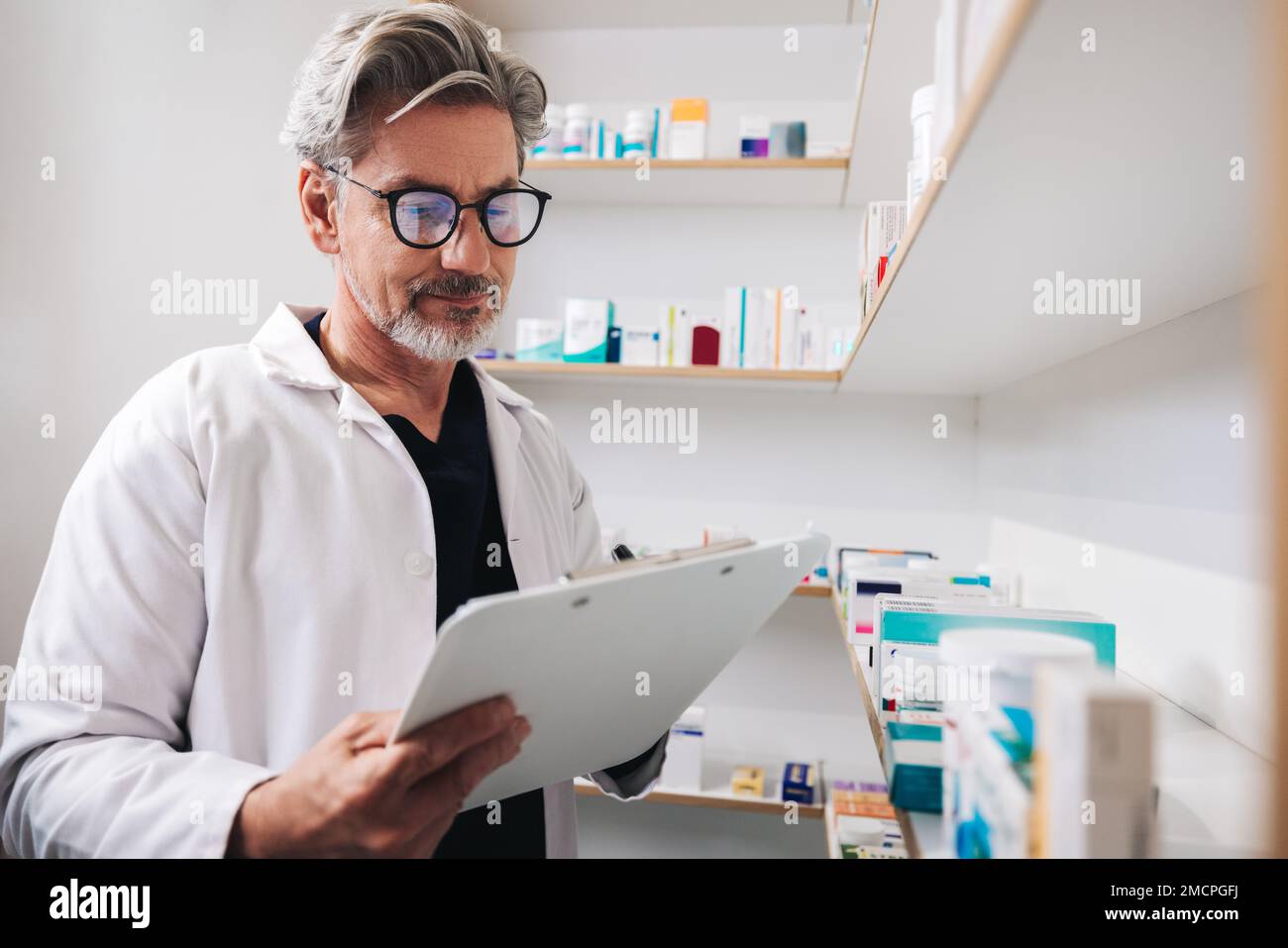 Pharmacist standing in a chemist and writing on a clipboard. Mature