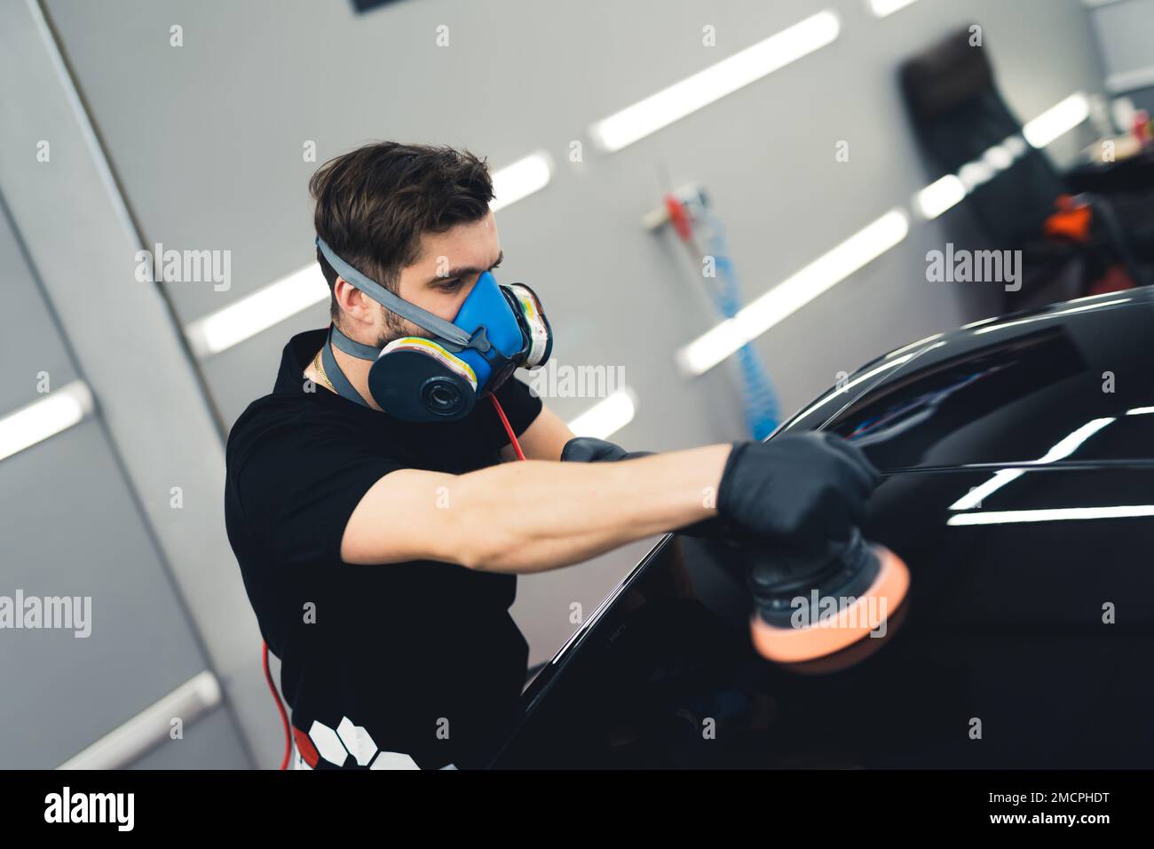 Car polishing service. Adult man in black t-shirt polishing black sports car varnish. High angle indoor shot. High quality photo Stock Photo