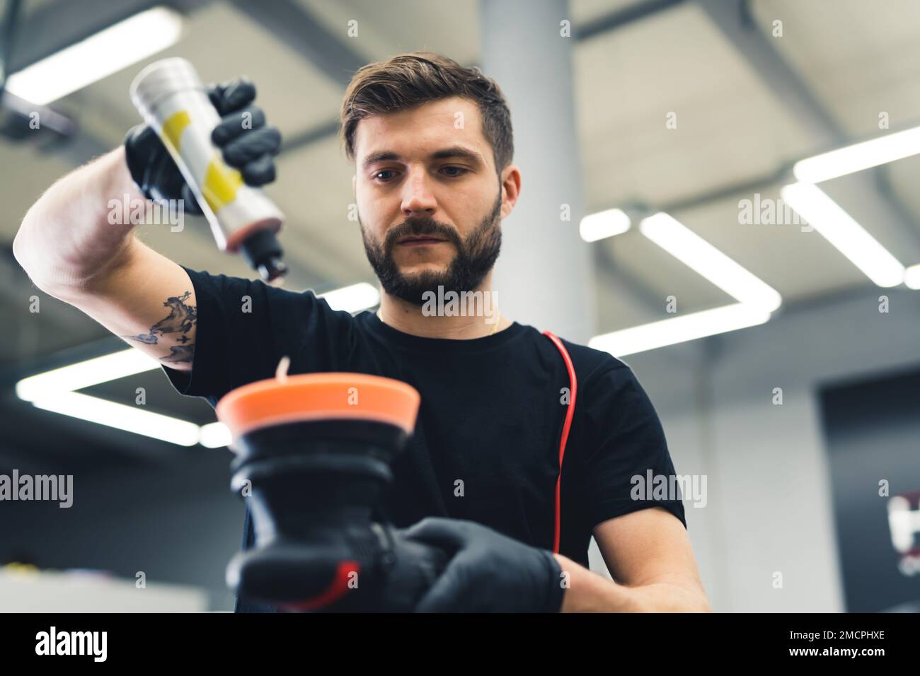Professional male car enthusiast pouring liquid onto orbital polisher