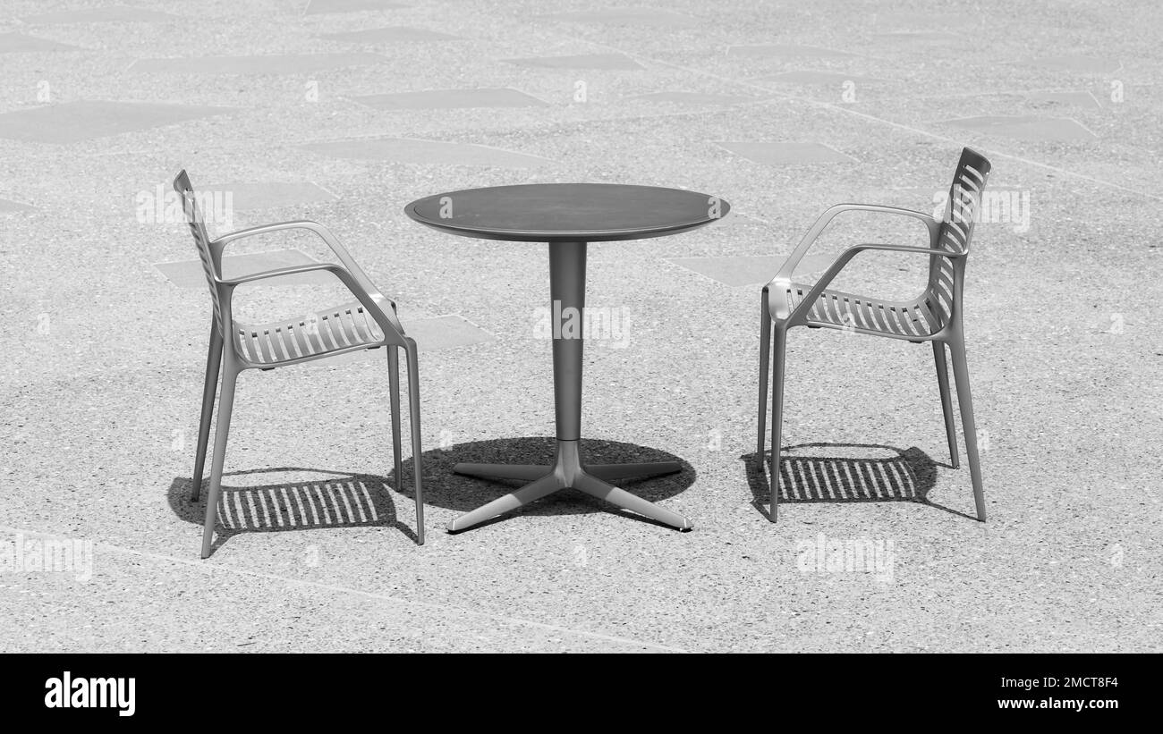 Black and white photo of two chairs at an empty table, selective focus