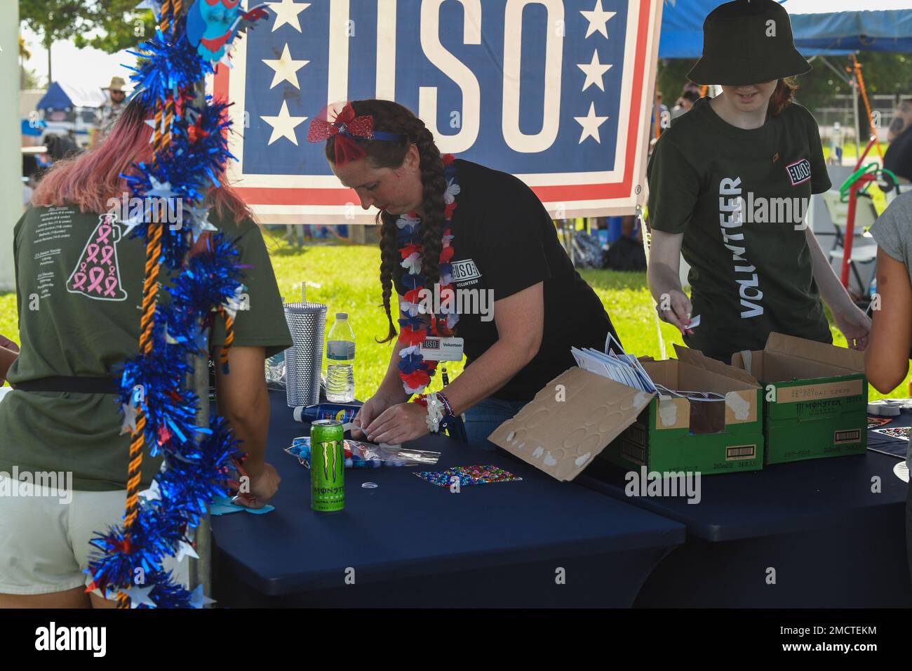Volunteers from the United Service Organization (USO) help make festive crafts at the Independence Day celebration at Kadena Air Base, Japan, July 9, 2022. The USO led the pack of vendors by making foam owls, handing out energy drinks, and informing festival-goers of the goodies to come in the remainder of the month. Stock Photo