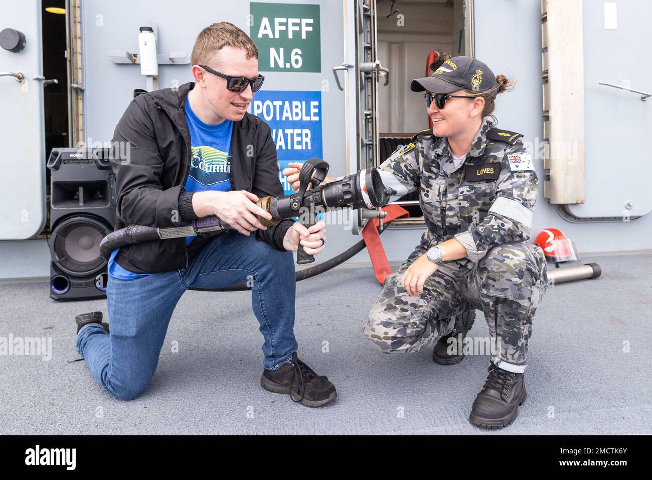 PEARL HARBOR July 9 2022 Able Seaman Aviation Support Abby Lowes explains the operation of a fire hose to a member of the public aboard Royal Australian Navy landing helicopter dock