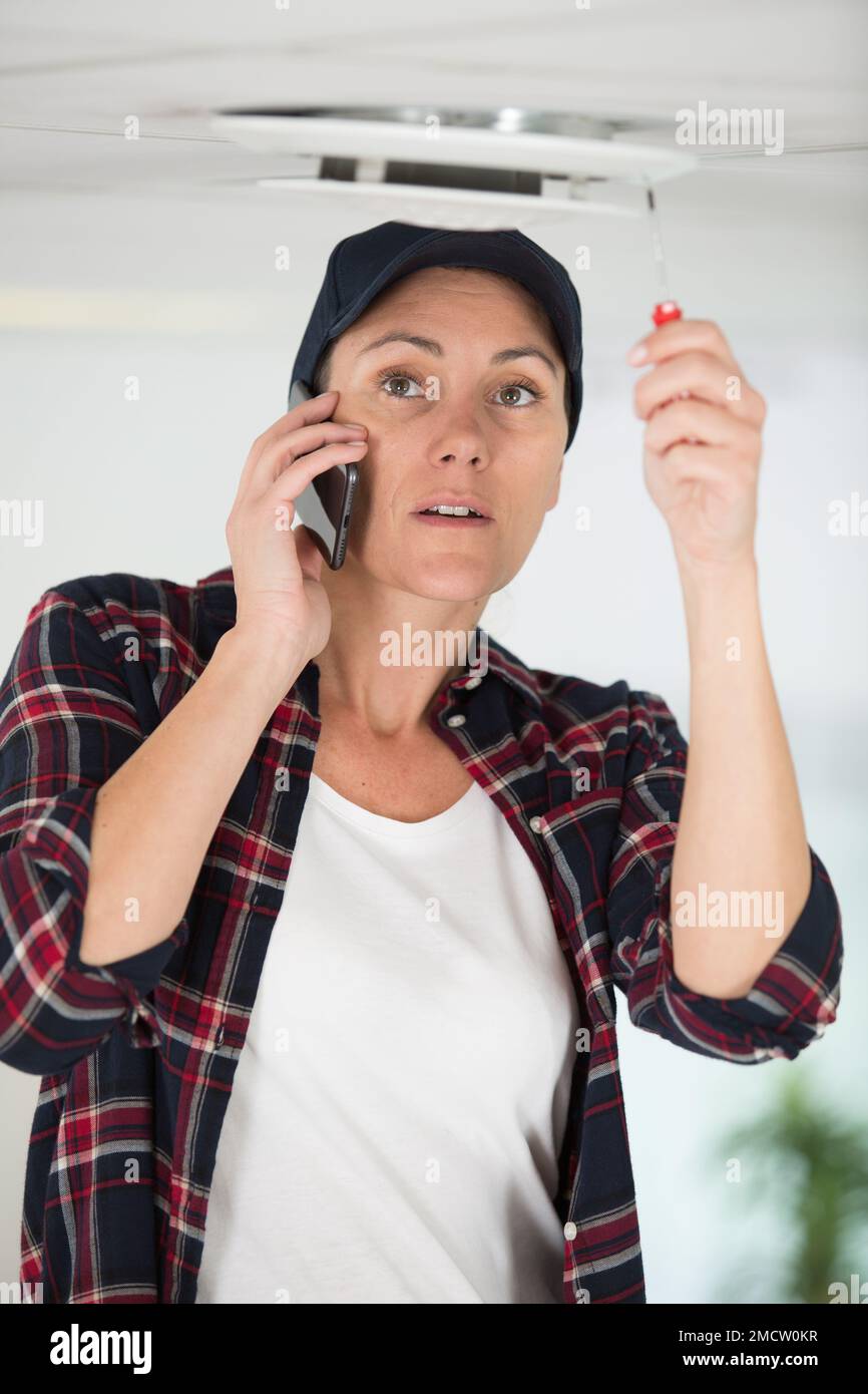 female worker on the phone screwing something on the ceiling Stock ...