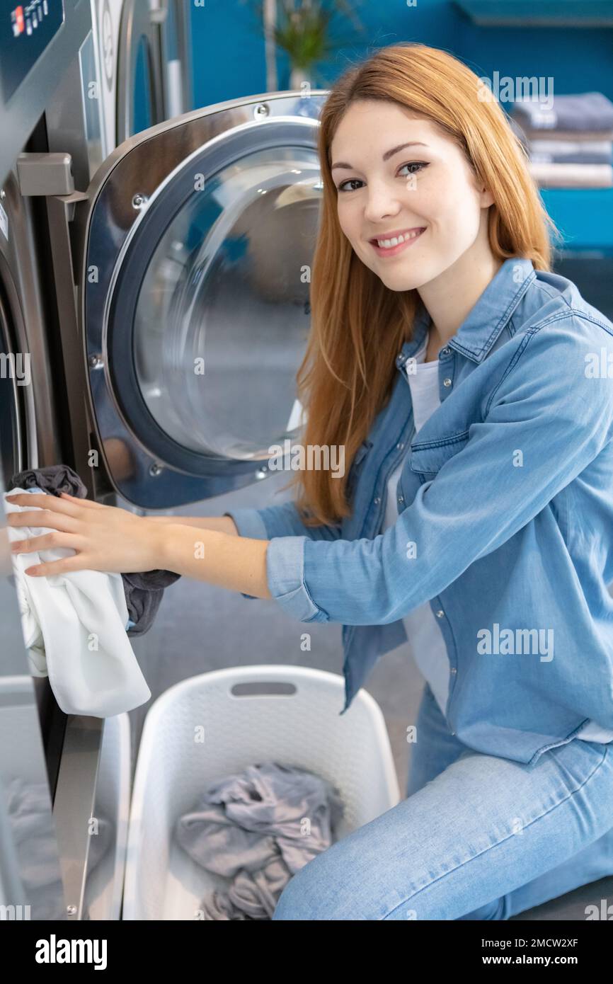 Young Woman Looking At Clean Clothes Out Of Washing Machine In Kitchen  Stock Photo - Alamy