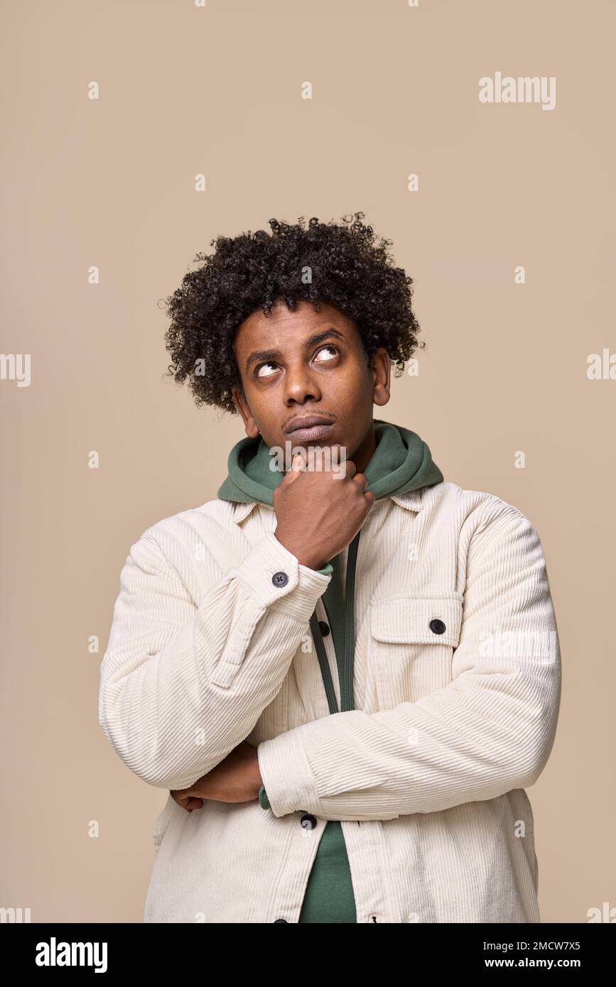 Thoughtful doubtful young African guy thinking isolated on beige. Vertical Stock Photo