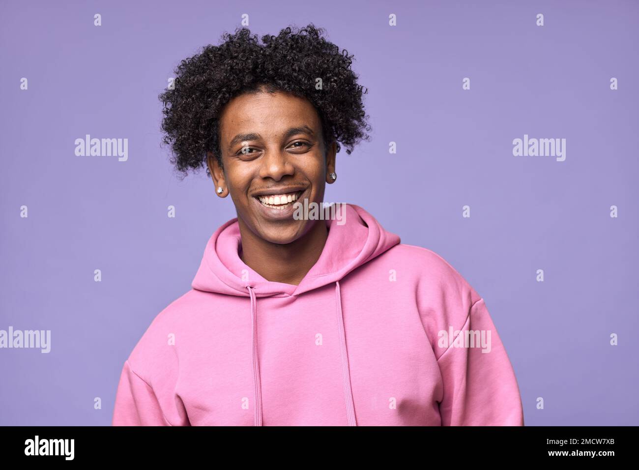 Young happy African American teen guy wearing pink hoodie isolated on purple. Stock Photo