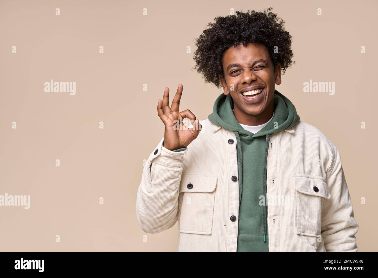 Happy cool African American teen guy showing ok winking isolated on beige. Stock Photo