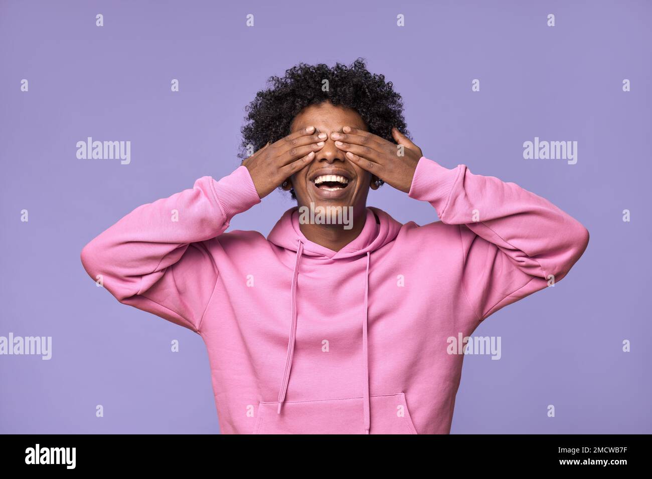 Happy African teen guy closing eyes with hands feels amazed waits for surprise. Stock Photo