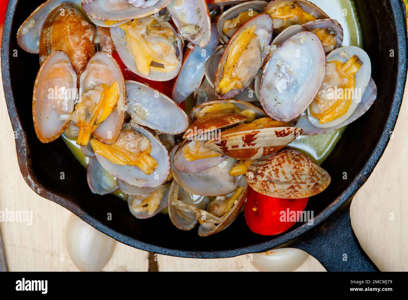 Fresh clams stewed on an iron skillet over wite rustic wood table Stock Photo