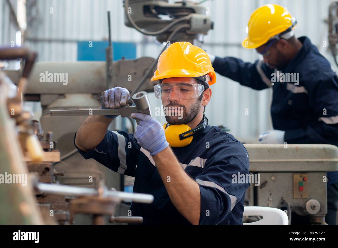 Young caucasian engineer man examining and measuring steel with expertise at lathe factory, worker or technician check and maintenance metal with prof Stock Photo
