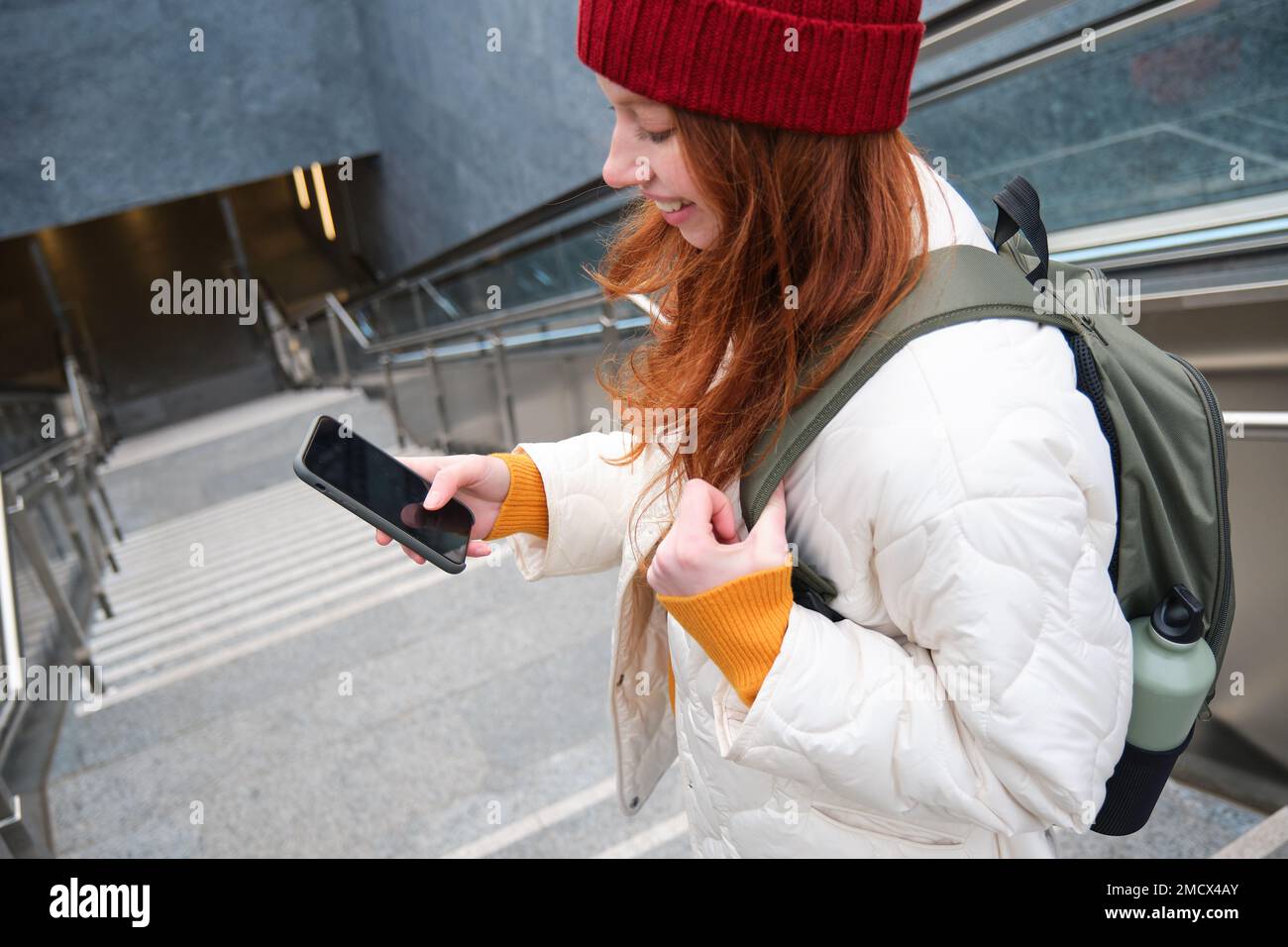 Smiling girl walking on stairs, using mobile phone, texting message on her way, using smartphone app map, follows route to destination place Stock Photo