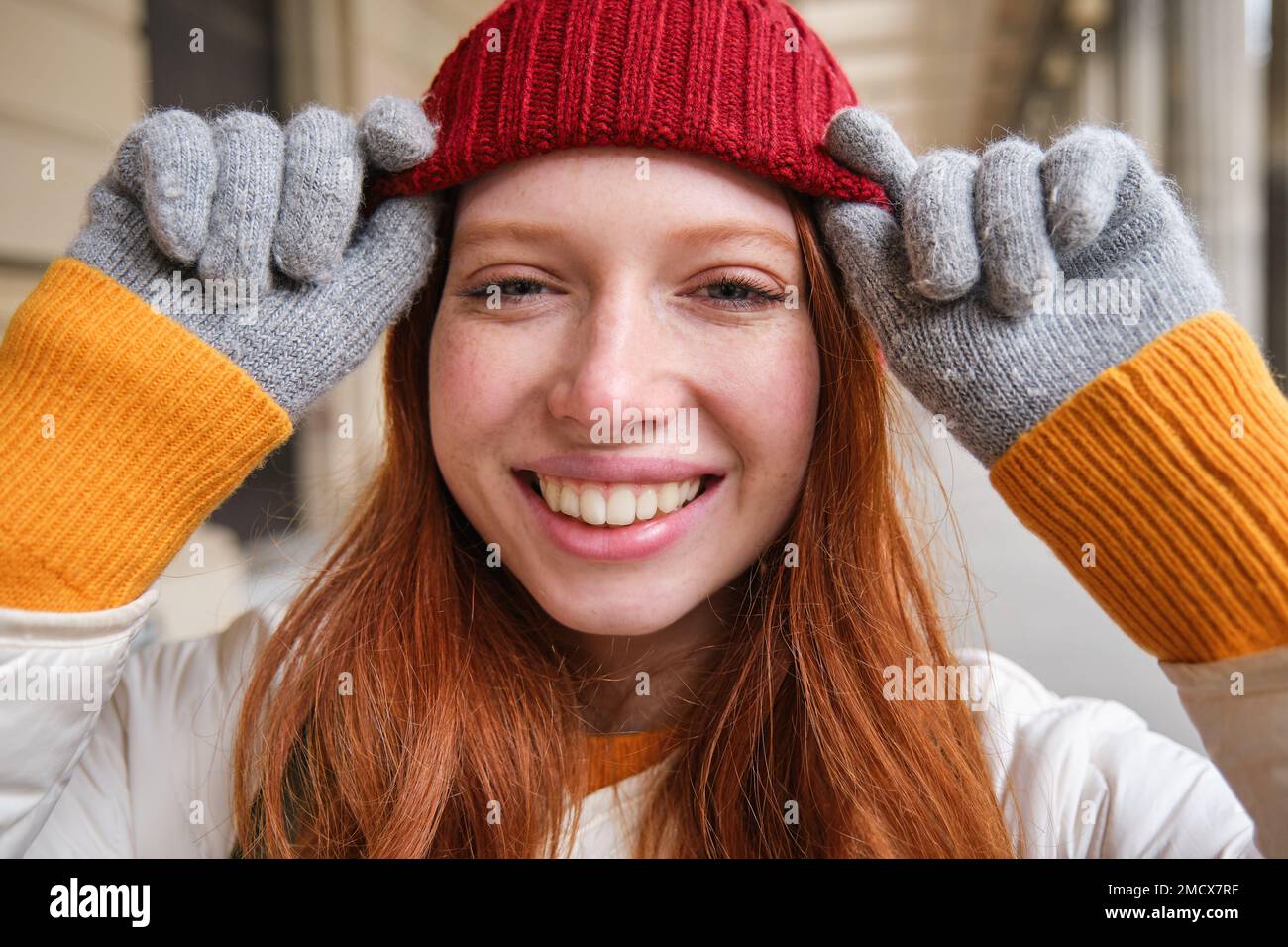 Headshot of happy redhead girl with freckles, wears red hat and gloves