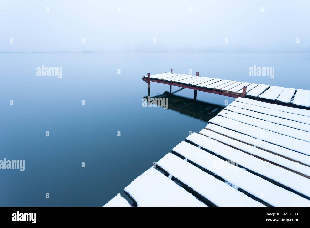 A snow-covered pier with a calm lake on a foggy day, Stankow, Poland Stock Photo