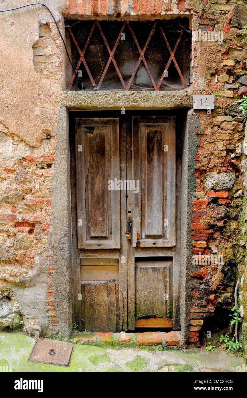 Vintage double wooden door set in a red brick rendered wall with a substantial grill above, Roccatederighi Mountain village, Tuscany, Italy, Stock Photo