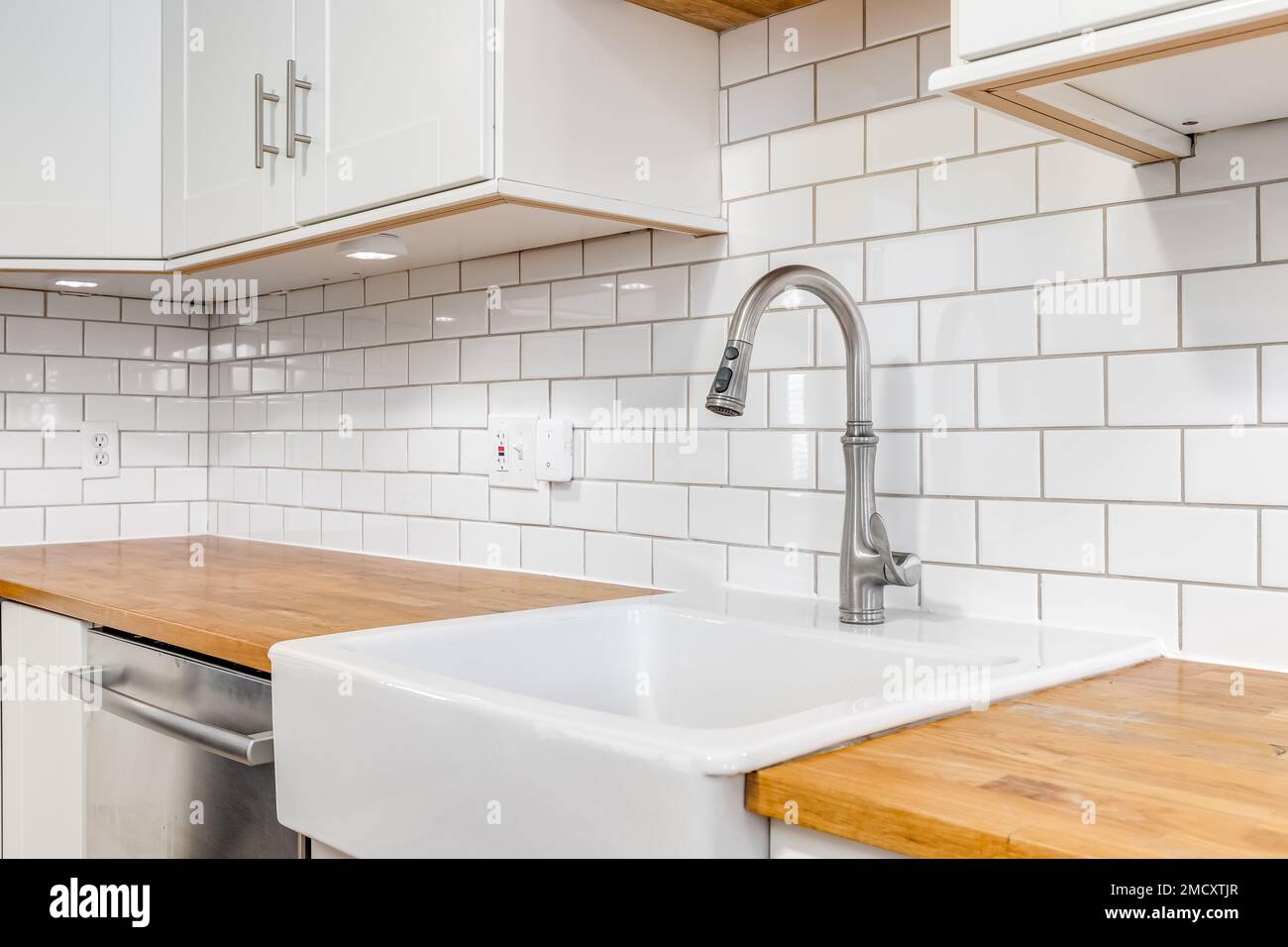 A kitchen sink detail with wood countertops, white an apron sink, and a subway tile