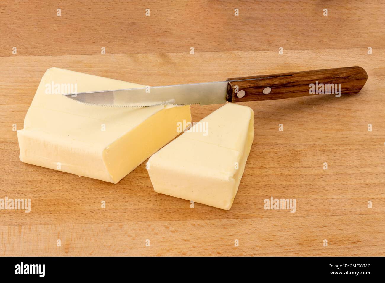 Block of butter cut with wooden handled knife on wooden cutting board Stock Photo