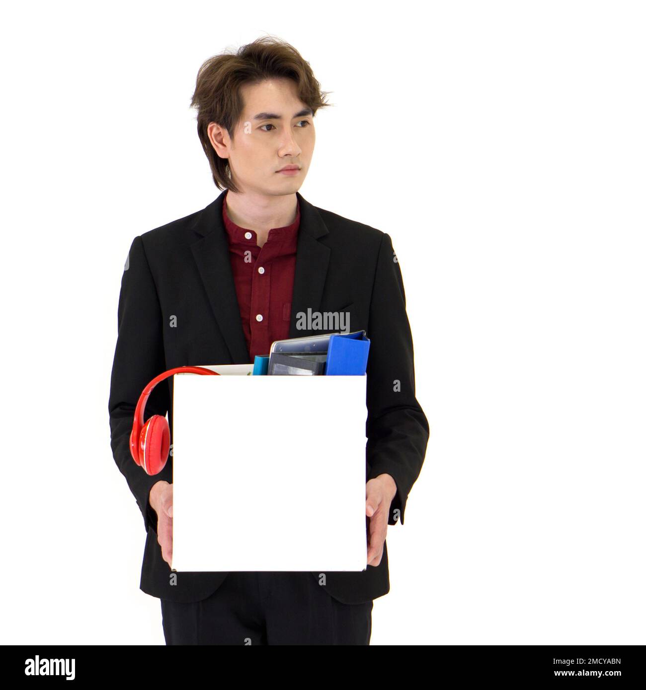 Young Asian businessman in black suit showing absent-minded, stressed and unhappy expression, holding paper box of belongings collected from office in Stock Photo